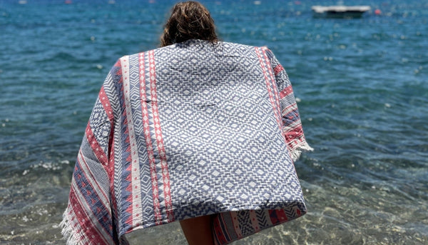 Person vid stranden med etnisk hamam handduk i geometriska mönster - turkisk peshtemal som strandlakan och sarong