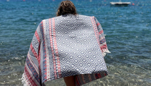 Person vid stranden med etnisk hamam handduk i geometriska mönster - turkisk peshtemal som strandlakan och sarong