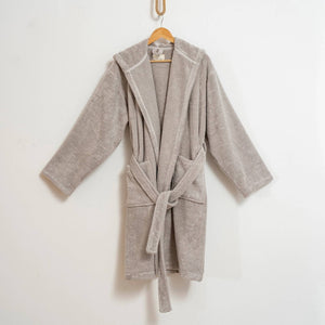 Beige badrock med pebble-struktur, huva och bälte hängande på trägalge