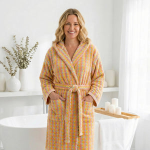 Kvinna i flerfärgad randig morgonrock med pompomstruktur och fickor i ljust badrum