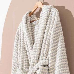 Grå rutmönstrad morgonrock med pompomstruktur hängande på trägalge