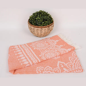 Hamamhandduk Mandala i orange med vitt mandalamönster och fransar, vikt med korg och grön växt