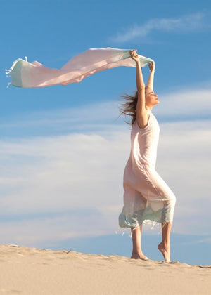 Sky tunn strandhandduk i rosa och mint hålls upp i vinden på sandstrand, lätt resehandduk och sarong