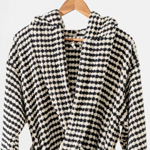 Svart-vit rutmönstrad morgonrock med pompomstruktur hängande på trägalge